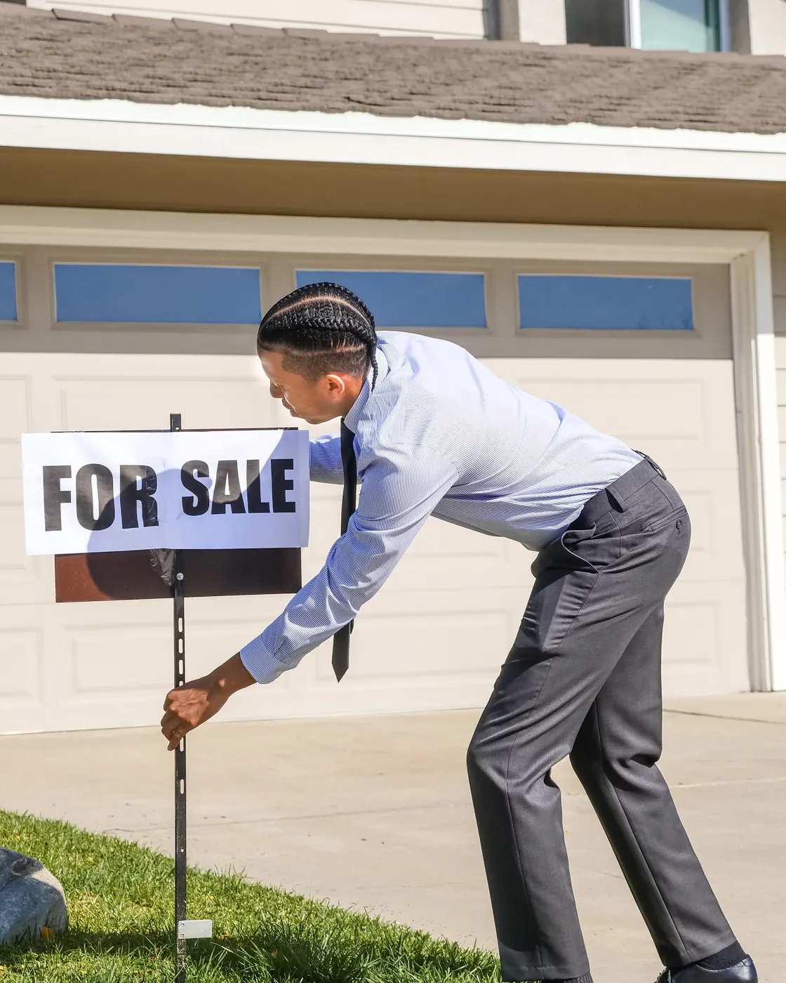A property negotiator setting a For Sale board outside a suburban home