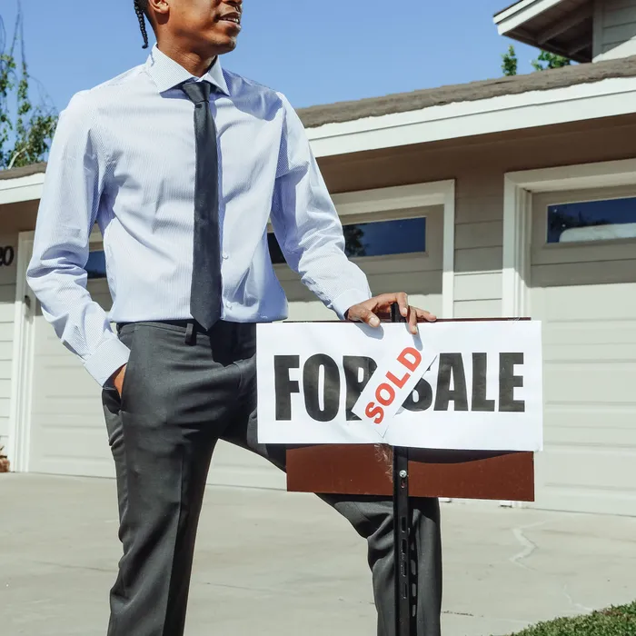 A negotiator holding a For Sale board marked Sold